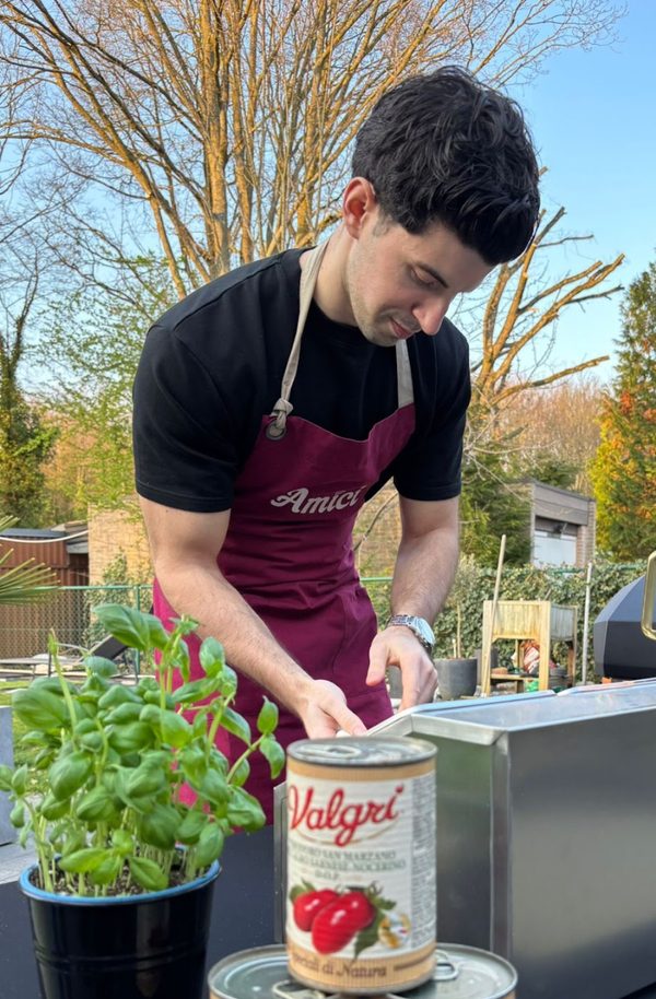 David van Amici bereidt verse ingrediënten in de buitenlucht voor pizza- en pastacatering, met een basilicumplant en San Marzano-tomaten, en toont authentieke Italiaanse keuken en ambachtelijke bereiding.