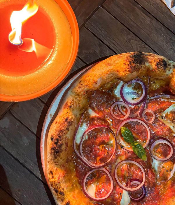 Ambachtelijke pizza met tomatensaus, gesmolten mozzarella, rode ui en verse basilicum, sfeervol geserveerd bij kaarslicht – perfect voor authentieke Italiaanse pizza- en pastacatering.
